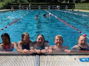 Kinder aufgereiht im Wasser am Beckenrand des Freibades