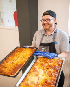 Küchenmitarbeiter hält zwei große Bleche mit Überbackenem