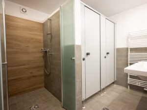 Moderner Waschraum mit zwei Toileten, begehbarer Dusche, Waschbecken und Heizkörper für Handtücher